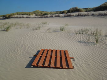 Deck chairs on sand against sky