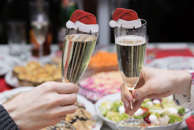 Cropped hands of friends toasting champagne flutes with santa hats at table