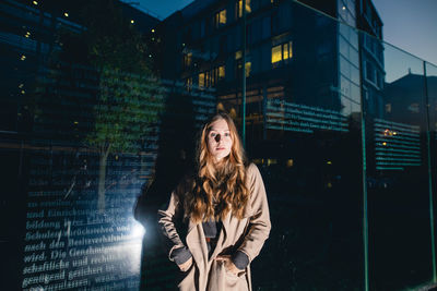 Portrait of young woman standing in illuminated city