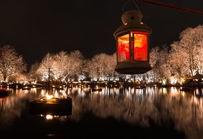 Illuminated building by lake against sky at night