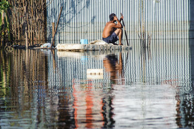 Full length of shirtless man sitting by lake