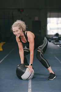 Portrait of smiling woman exercising with medicine ball while at gym