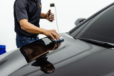 Midsection of man holding mobile phone while standing by car