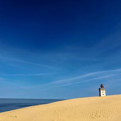 Lighthouse on beach by sea against blue sky