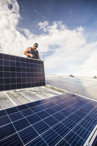 Low angle of electrician installing solar panels on roof.