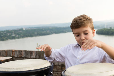 Boy playing bongo against river