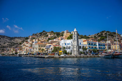 Sea by buildings in town against blue sky