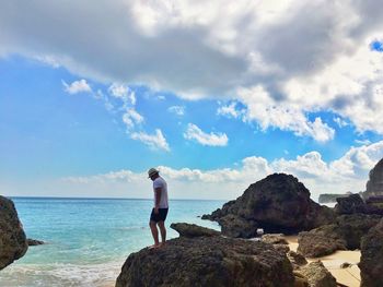 Man standing on rock by sea against blue sky