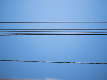 Low angle view of power lines against clear blue sky