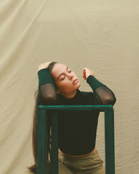 Woman with hand in hair standing against beige backdrop