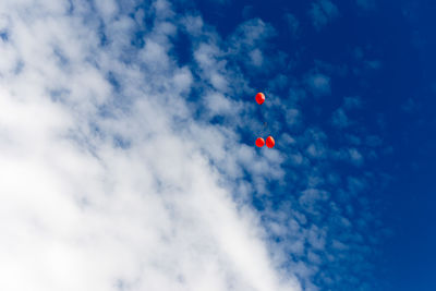 Low angle view of red balloons flying against blue sky