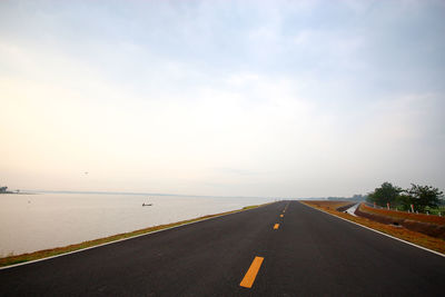 Empty road by sea against sky