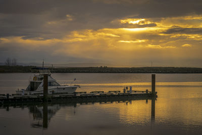 Yacht moored by jetty in lake against cloudy sky during sunset