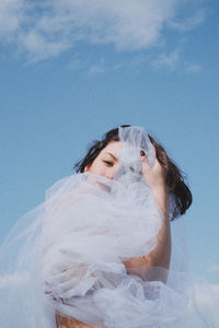 Low angle portrait of young woman in white dress against sky