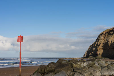 Lighthouse on rocks by sea against sky