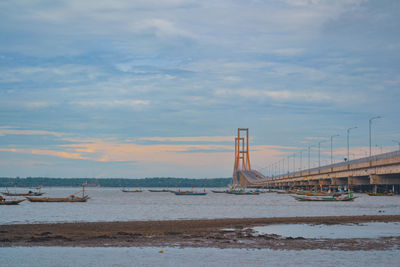 View of suspension bridge over sea against cloudy sky