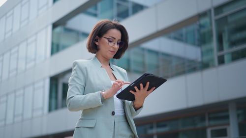 Vertical view of the beautiful young woman using tablet computer while walking through night city