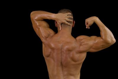 Rear view of shirtless muscular man flexing muscles against black background
