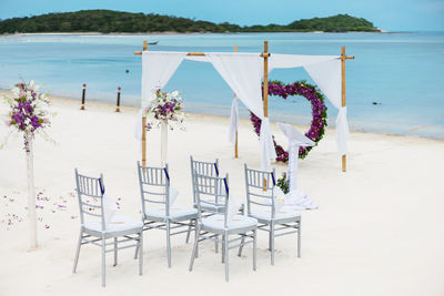 Empty chairs and table at beach against sky