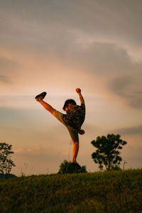 Rear view of kid practice kungfu on field against sky during sunset