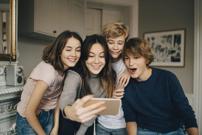 Cheerful friends taking selfie through smart phone while standing at home