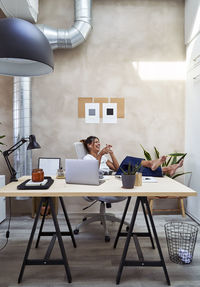 Happy businesswoman wearing wireless in-ear headphones talking on phone at home