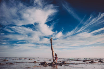 Rear view of woman standing by tree trunk at sea against sky