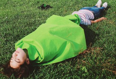 Woman wrapped in green blanket sleeping with female friend on grassy field