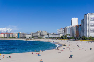 People on beach by buildings against clear blue sky