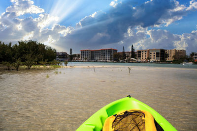 Sun shines through the clouds over a green kayak in the water of new pass in bonita springs, florida