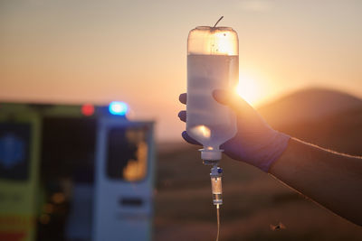 Close-up hand of paramedic holding infusion set against ambulance car of emergency medical service.