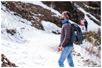 Side view of young man with backpack standing on snowcapped mountain