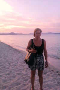 Portrait of woman with purse standing at sandy beach during sunset