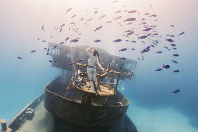 Woman on abandoned boat surrounded by fish in sea