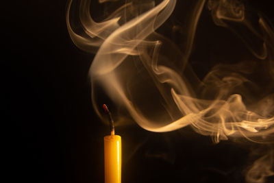 Close-up of candle emitting smoke against black background