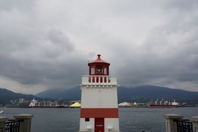 Lighthouse by sea and buildings against sky