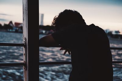 Rear view of sad man standing by railing in boat on lake