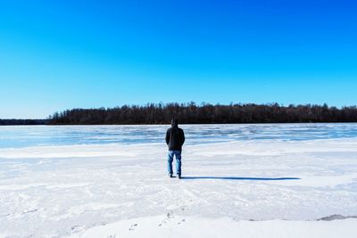 Rear view of man looking at frozen lake against clear blue sky