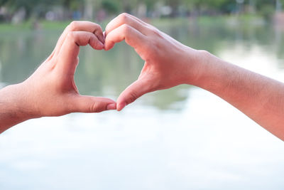 Cropped hands of homosexual couple making heart shape by lake