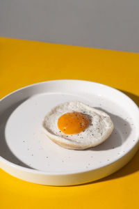 Zine styled creative round plate with fried egg on a yellow table with hard shadows. 