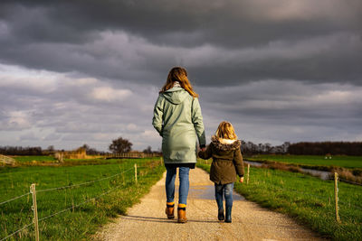 Rear view of mother and daughter walking on road against sky