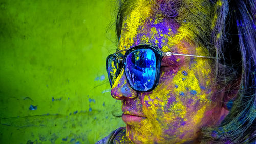 Close-up of messy woman with powder paint on face wearing sunglasses during holi
