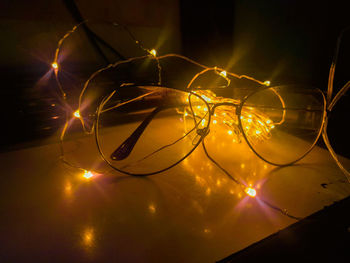Close-up of illuminated string lights with eyeglasses on table in darkroom