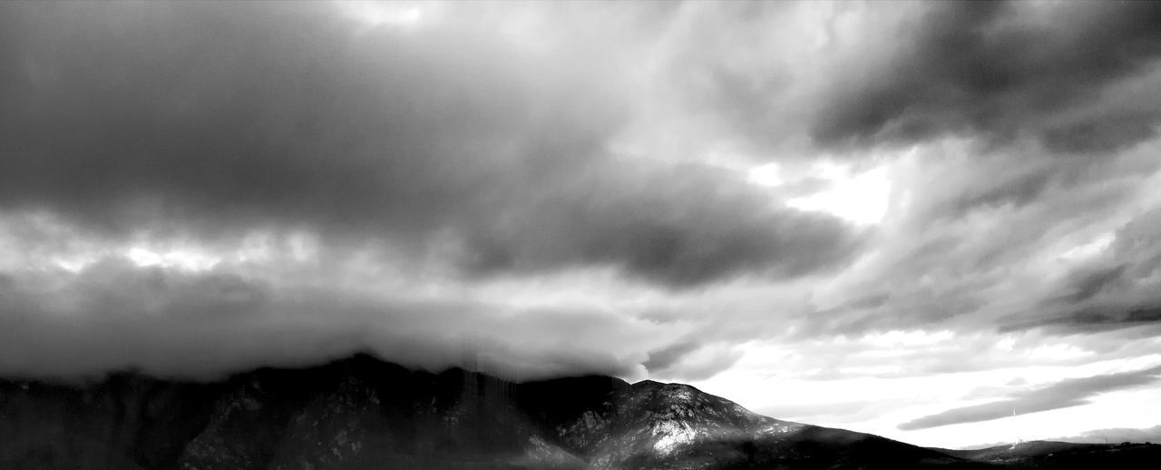 LOW ANGLE VIEW OF SUNLIGHT STREAMING THROUGH CLOUDS OVER MOUNTAIN