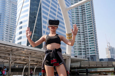 Woman wearing 3-d glasses while gesturing against building