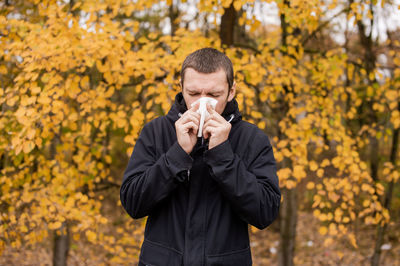 A man in a jacket is standing on the street and holding a napkin near his nose