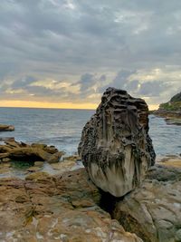 Rock formation on beach against sky during sunset
