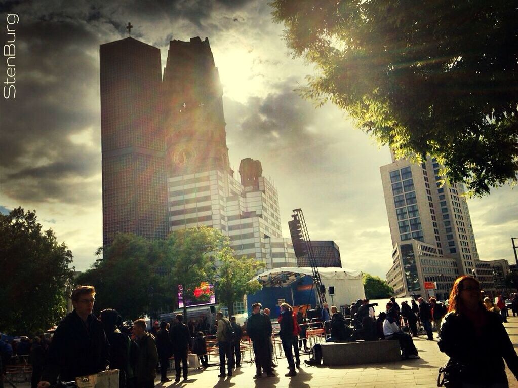 building exterior, architecture, large group of people, built structure, city, men, person, lifestyles, tall - high, skyscraper, sky, city life, leisure activity, modern, tower, cloud - sky, tree, office building, mixed age range