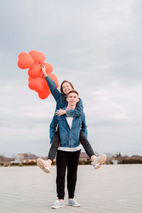 Full length of happy man with balloons standing against sky