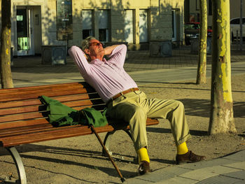 Man in colourful clothes sleeping on bench in the sun 